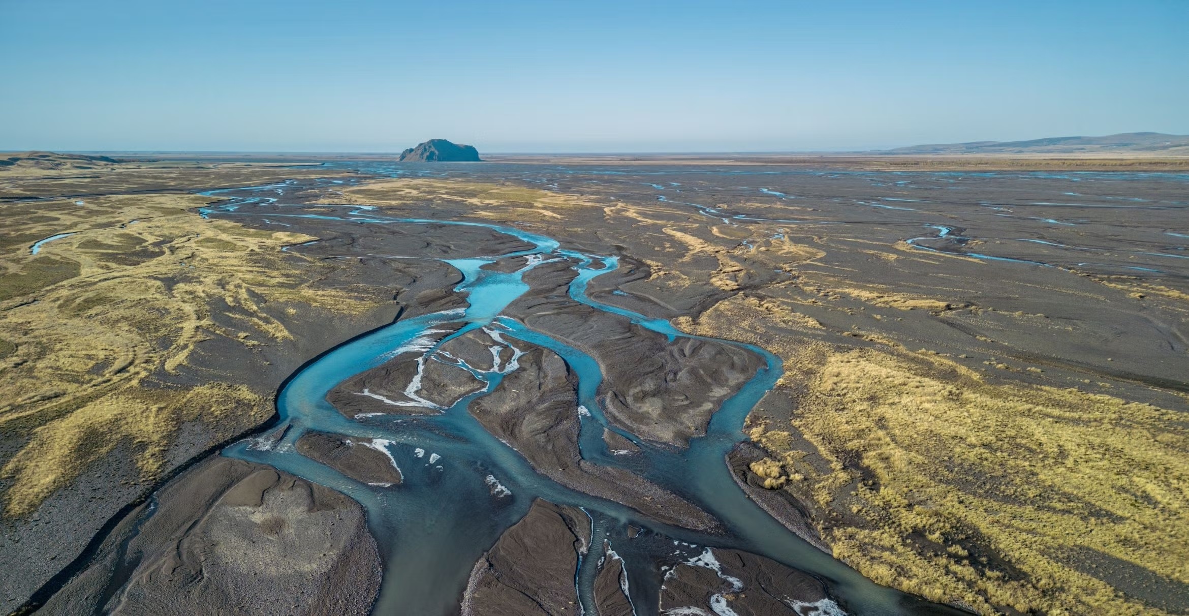 Aerial view of dry land with winding blue streams and a distant rock formation. Photo credit: Luca Ronchi via iStock.