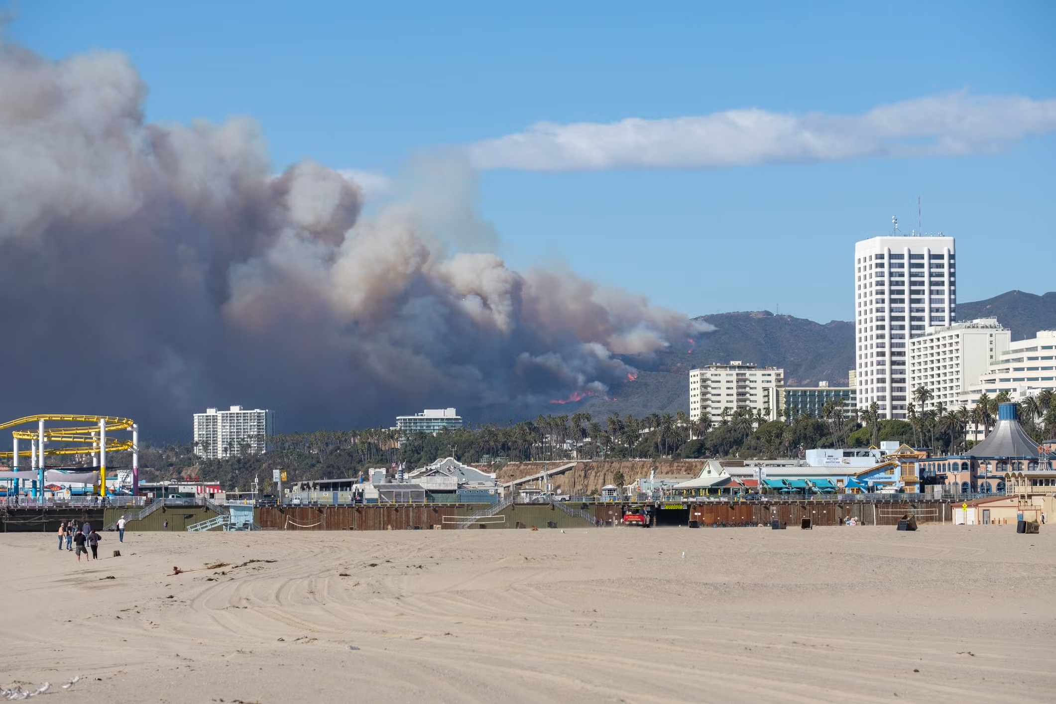 Smoke from a wildfire rises from hills behind beachfront buildings in Santa Monica.