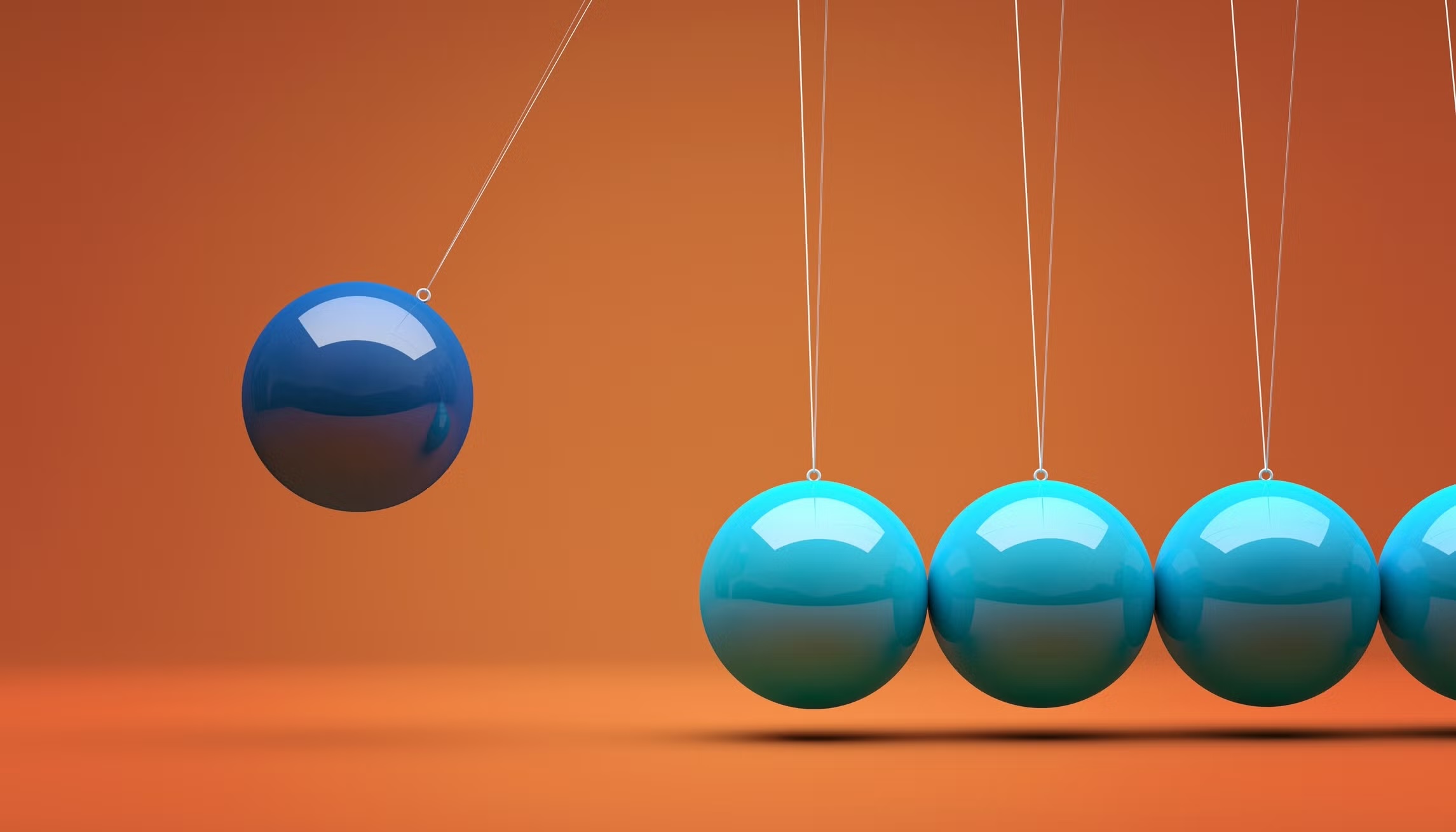 A Newton's Cradle demonstration with five steel spheres suspended in a line, illustrating the principles of conservation of momentum and energy. The leftmost blue sphere is pulled back and held, ready to strike the four stationary light-blue spheres.