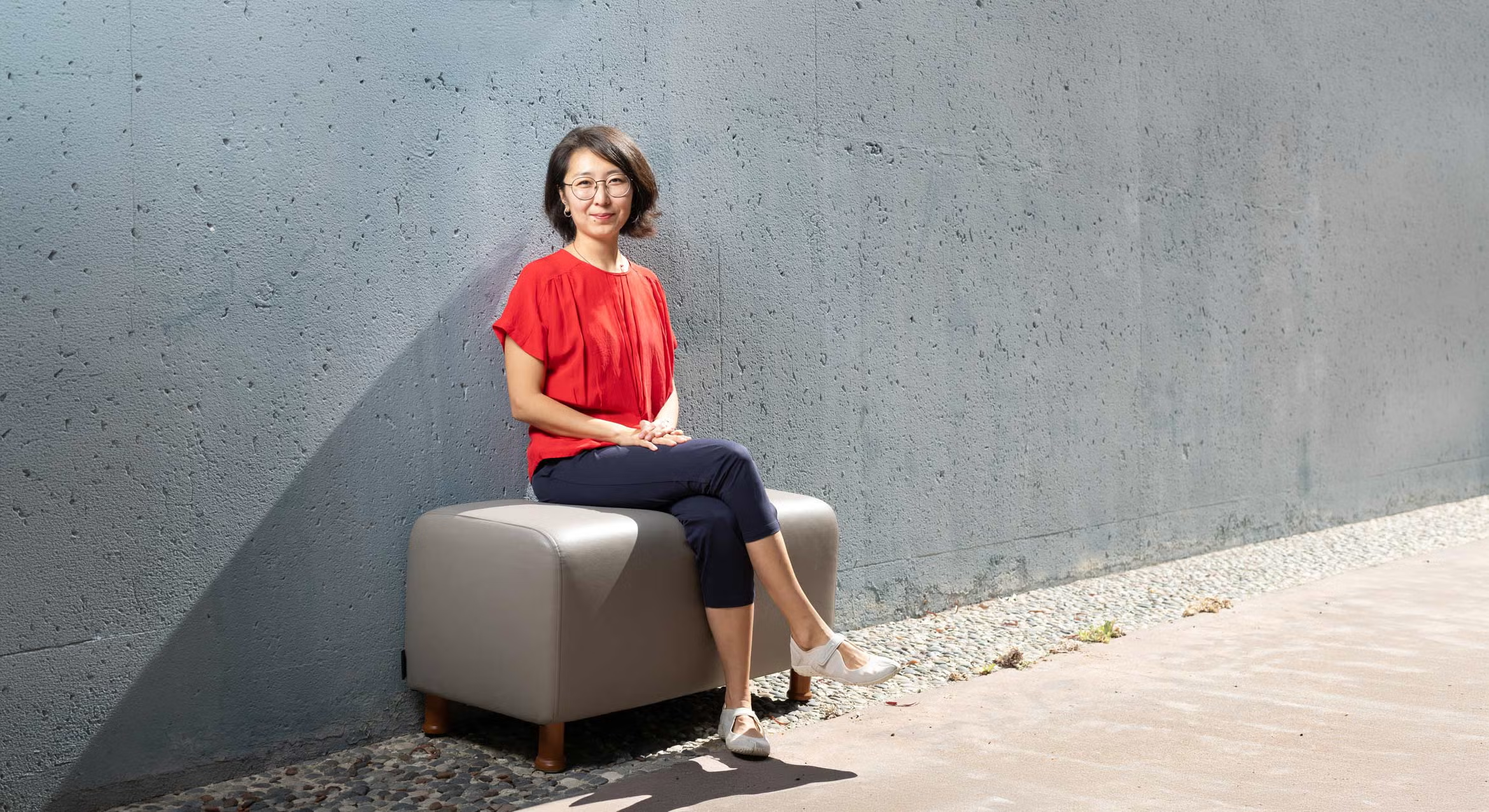 Wenfei Xu sits outdoors on a bench against a grey concrete wall for a portrait.