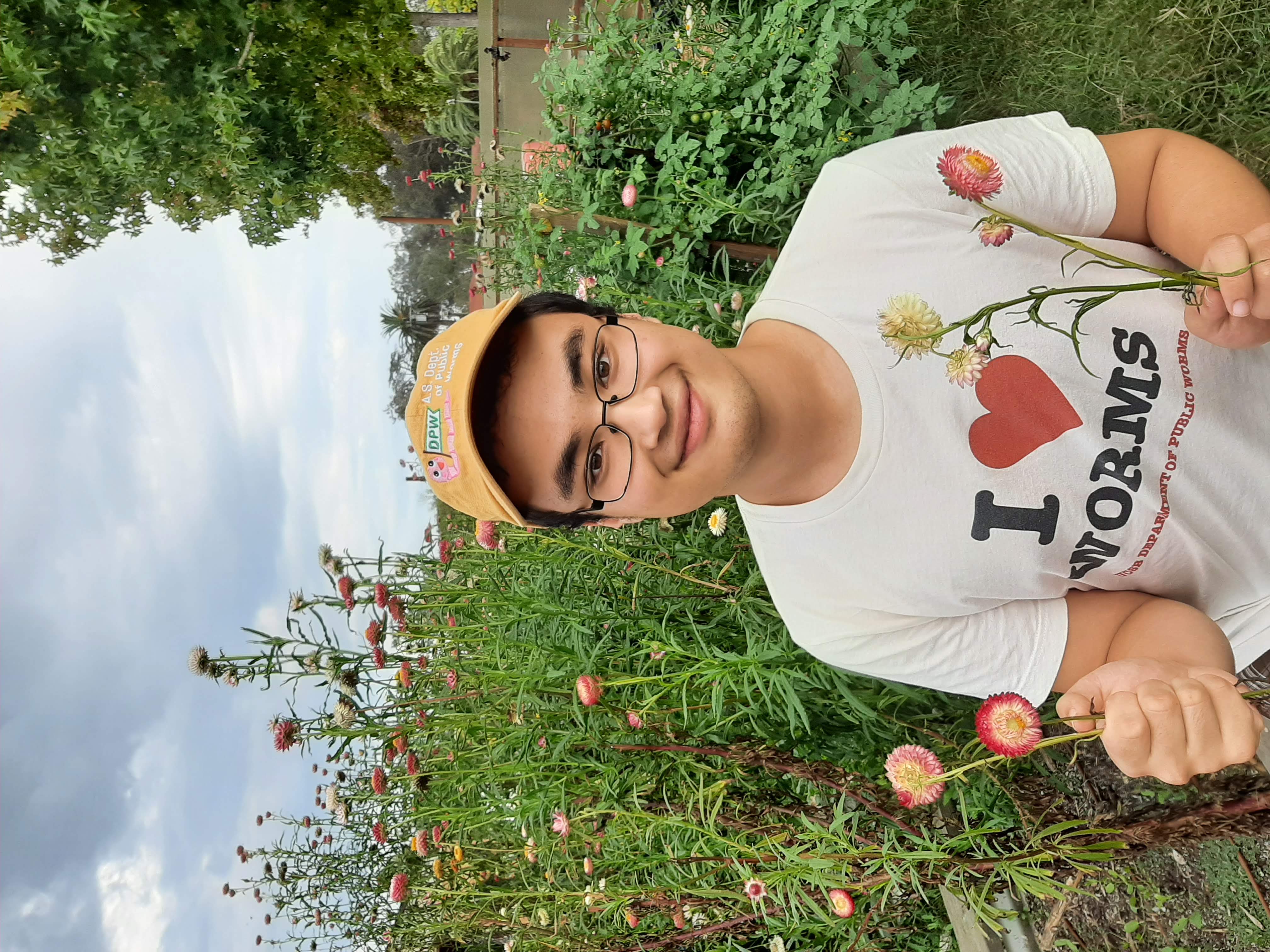 Ben Wollack, a UC Santa Barbara Environmental Studies student, smiling outdoors while holding a handful of pink and white flowers.