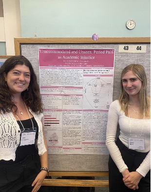 Undergraduate researchers Sofía Lebensohn and Kailey Reed standing and smiling in front of their academic research poster titled 'Unaccommodated and Unseen: Period Pain as Academic Injustice'.